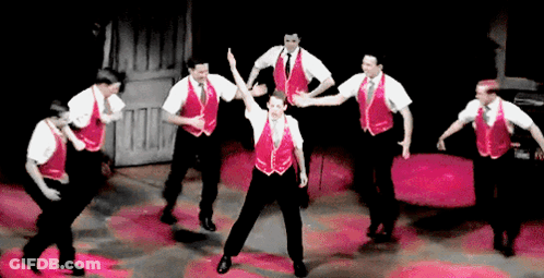 A Group Of Men Wearing Red Vests And White Shirts Are Dancing On A Stage GIF