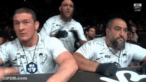 A Group Of Men Wearing White Ufc Shirts Are Watching A Fight GIF
