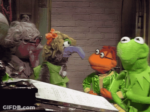 A Group Of Muppets Including Kermit The Frog Are Standing Around A Sheet Of Paper GIF