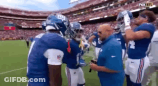 A Group Of New York Giants Football Players Are Standing On A Field Talking To Each Other . GIF