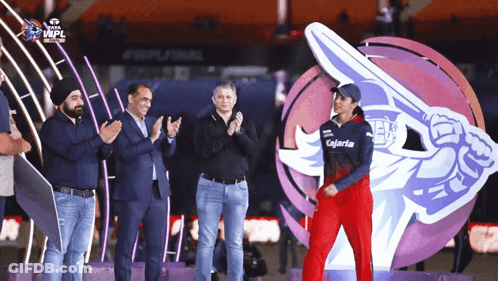 A Group Of People Applaud A Woman Wearing A Kalaria Shirt GIF