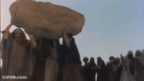 A Group Of People Are Carrying A Large Rock On Their Heads GIF