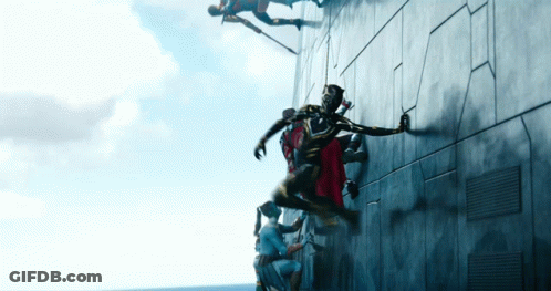 A Group Of People Are Climbing Up A Wall And One Of Them Is Wearing A Red Cape GIF