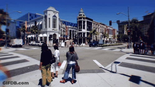 A Group Of People Are Crossing A Street In Front Of A Building That Says ' O'neill ' On It GIF