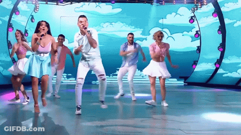 A Group Of People Are Dancing And Singing On A Stage With A Blue Background GIF