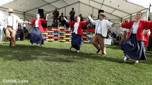 A Group Of People Are Dancing In A Field In Front Of A Tent GIF