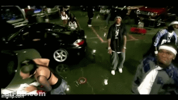 A Group Of People Are Dancing In A Parking Lot With Cars In The Background . GIF