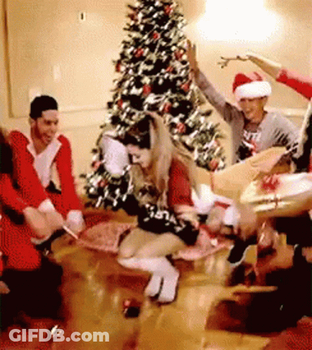 A Group Of People Are Dancing In A Room In Front Of A Christmas Tree . GIF