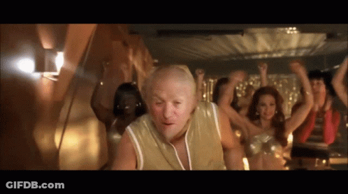 A Group Of People Are Dancing In A Room With A Bald Man In The Foreground GIF