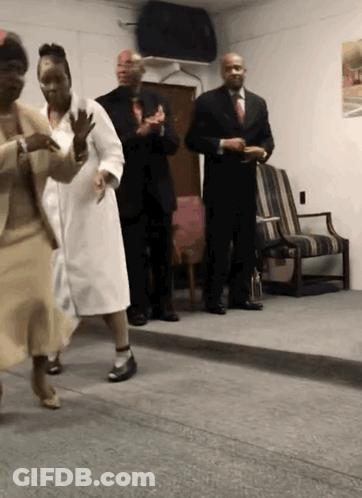 A Group Of People Are Dancing In A Room With A Man In A Suit GIF