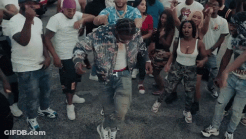 A Group Of People Are Dancing In A Street With A Man Wearing A Floral Jacket GIF