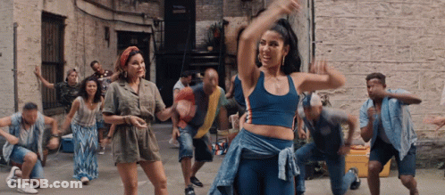A Group Of People Are Dancing In An Alleyway In Front Of A Brick Building GIF