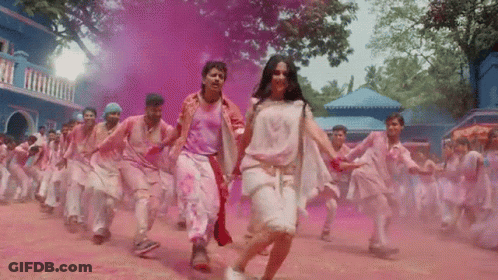 A Group Of People Are Dancing In Front Of A Blue Building Covered In Pink Powder GIF