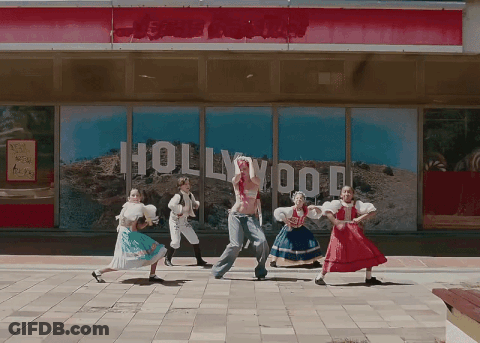 A Group Of People Are Dancing In Front Of A Building That Says Hollywood GIF
