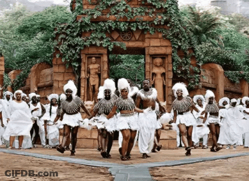 A Group Of People Are Dancing In Front Of A Statue . GIF