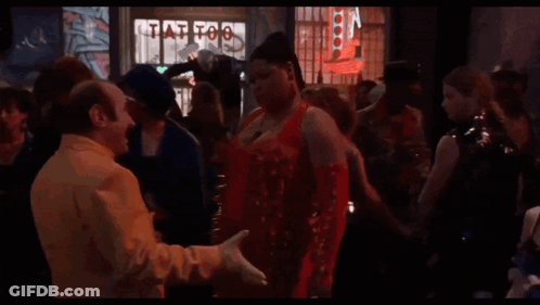 A Group Of People Are Dancing In Front Of A Tattoo Shop Sign GIF
