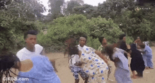 A Group Of People Are Dancing In The Dirt In A Field . GIF