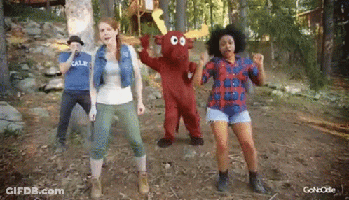 A Group Of People Are Dancing In The Woods With A Mascot In The Middle . GIF