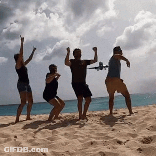 A Group Of People Are Dancing On A Beach While A Plane Is Flying In The Background . GIF