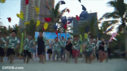 A Group Of People Are Dancing On A Beach With Balloons In The Air GIF