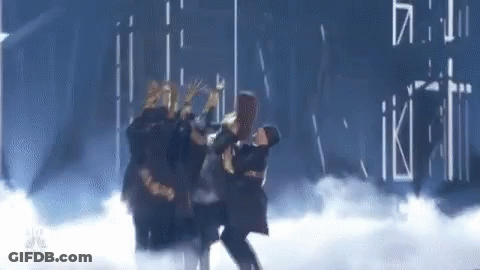 A Group Of People Are Dancing On A Stage In A Dark Room . GIF