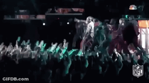 A Group Of People Are Dancing On A Stage In Front Of A Crowd At A Football Game . GIF