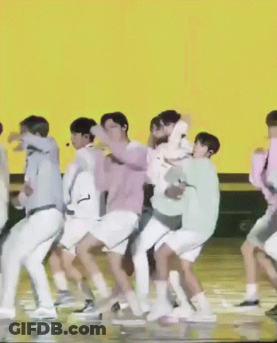 A Group Of People Are Dancing On A Stage In Front Of An Orange Background GIF
