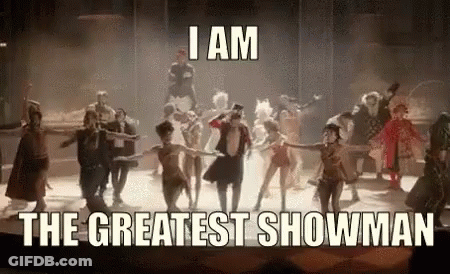 A Group Of People Are Dancing On A Stage With The Words `` I Am The Greatest Showman '' Written Above Them . GIF