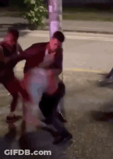A Group Of People Are Fighting On The Side Of A Street . GIF