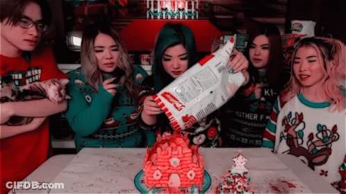 A Group Of People Are Gathered Around A Gingerbread House And One Of The Girls Is Holding A Bag Of Kraft Macaroni And Ch GIF