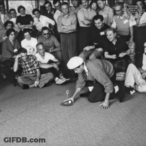 A Group Of People Are Gathered Around A Man Kneeling On The Floor Playing A Game With A Ball GIF