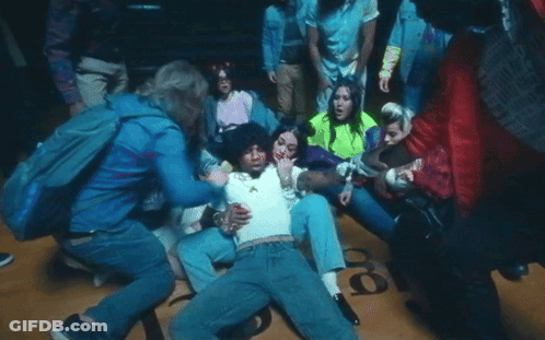 A Group Of People Are Gathered Around A Man Laying On The Floor With The Number 18 On The Ground GIF