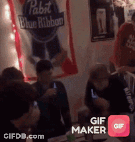 A Group Of People Are Gathered Around A Table With A Pabst Blue Ribbon Banner Behind Them GIF
