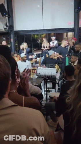 A Group Of People Are Gathered In A Room With A Sign That Says ' One Camp ' In The Corner GIF