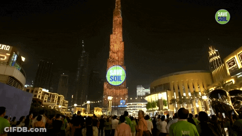 A Group Of People Are Gathered In Front Of A Tower That Says Save Soil On It GIF