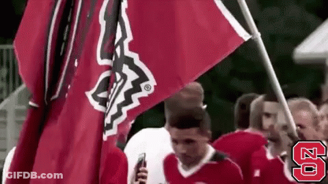 A Group Of People Are Holding A Red Flag And A Man Is Holding A Cell Phone . GIF