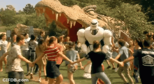A Group Of People Are Holding Hands In Front Of A Statue Of A Dinosaur And A Robot GIF