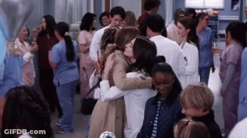 A Group Of People Are Hugging Each Other In A Crowded Room . GIF
