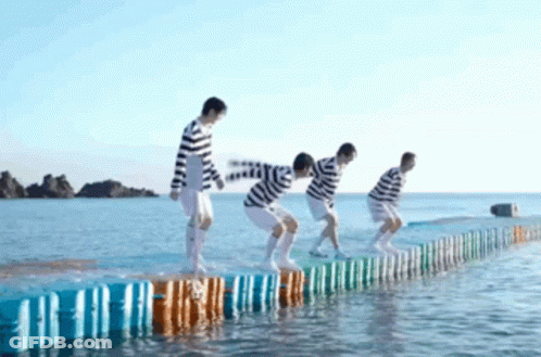 A Group Of People Are Jumping Over A Fence Into The Water . GIF