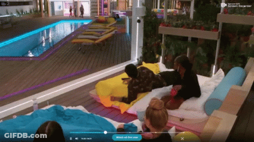 A Group Of People Are Laying On A Bed In Front Of A Pool And A Screen That Says " Watch Out For Now " GIF