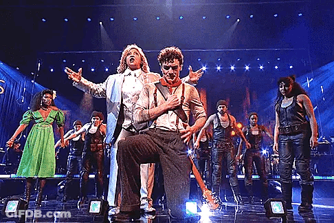 A Group Of People Are Performing On A Stage Including A Man Holding A Guitar . GIF