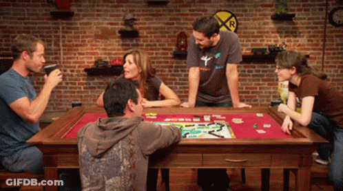 A Group Of People Are Playing A Board Game With A Railroad Crossing Sign In The Background GIF