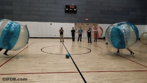 A Group Of People Are Playing A Game Of Bubble Soccer In A Gym With A Scoreboard That Says 7:40 GIF