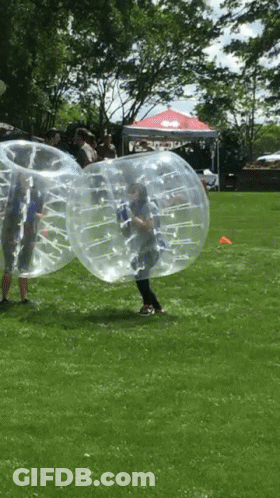 A Group Of People Are Playing Bubble Soccer In A Grassy Field GIF