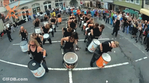 A Group Of People Are Playing Drums On A Street With A Sign That Says ' Rhythm ' GIF
