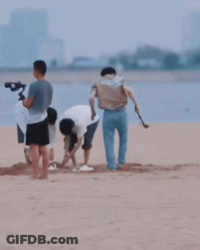 A Group Of People Are Playing In The Sand On A Beach GIF