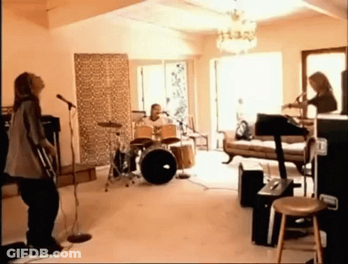 A Group Of People Are Playing Instruments In A Living Room While A Woman Sings Into A Microphone . GIF