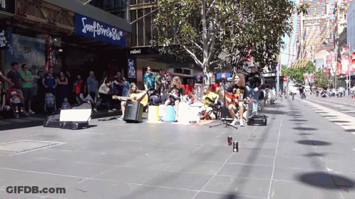 A Group Of People Are Playing Instruments On A Sidewalk In Front Of A Sign That Says Souldriver Shop GIF