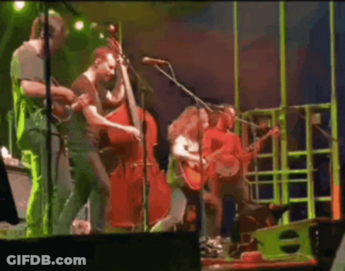 A Group Of People Are Playing Instruments On A Stage And Singing Into Microphones . GIF