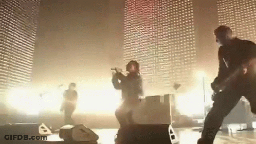 A Group Of People Are Playing Instruments On A Stage In Front Of A Wall . GIF